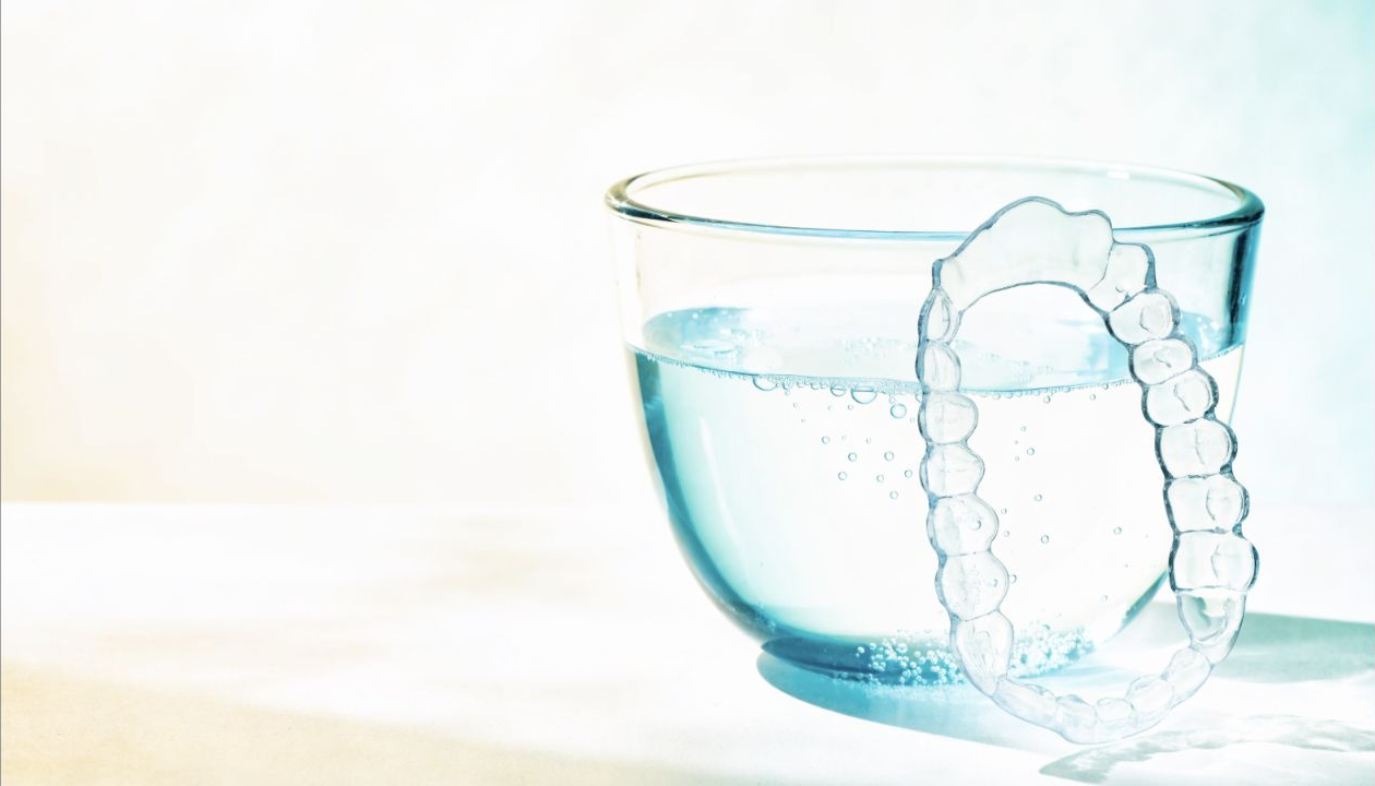 Transparante uitneembare retainer naast een reinigingsbad met water